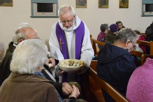 Jesuit Father Richard Shortall, a missionary of mercy for the Jubilee Year of Mercy, offers rocks to parishioners during an evening prayer service at St. Patrick and St. Brigid Church in Cooranbong, Australia, May 26. He invited parishioners to reflect on any weights they may have and then to place the rocks in a bucket on the altar as a sign of letting them go. Father Shortall, one of two missionaries of mercy in Australia, is traveling throughout the Maitland-Newcastle Diocese in a motor home to rural parishes that have no resident priest. (CNS photo/Fiona Basile) See AUSTRALIA-MISSIONARY-MERCY June 7, 2016.