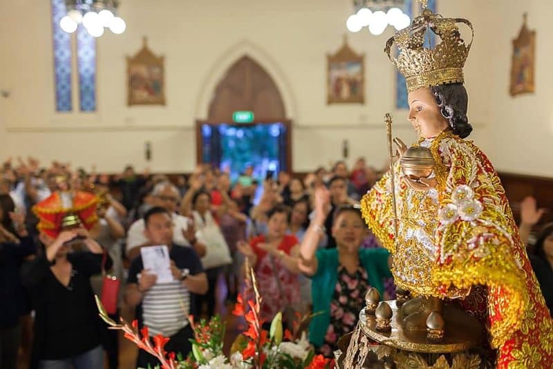 A statue of the Santo Niño, with devotees in the background, at St Patrick’s Cathedral 
in Auckland.