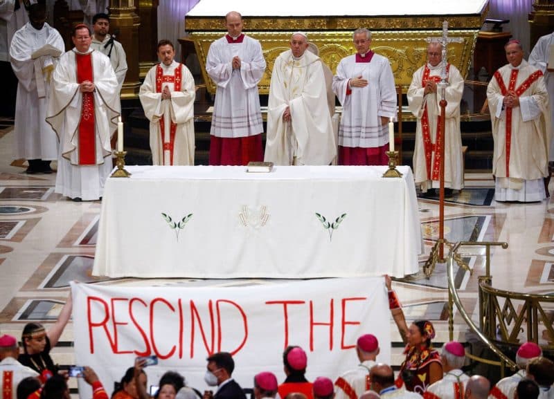 Indigenous people hold a banner calling on Pope Francis to "rescind the doctrine," an apparent reference to the so-called Doctrine of Discovery, a collection of old papal teachings that encouraged explorers to colonize and claim the lands of any people who were not Christian, placing both the land and the people under the sovereignty of European Christian rulers. The incident occurred during a papal Mass at the National Shrine of Sainte-Anne-de-Beaupré in Quebec July 28, 2022. (CNS photo/Guglielmo Mangiapane, Reuters)
